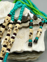 Load image into Gallery viewer, These stylish skull earrings are perfect for adding a unique flair to any outfit. Whether you're looking for a Dia De Los Muertos accessory or simply looking to draw inspiration, these goth pieces perfectly capture the vampire goth, witchy, dark, Chingona Cabrona, Latina Chicana styles. Skull-shaped bone beads adorned with dark brown, turquoise, and gold beaded earrings make up this unique set of earrings. Measurements: 1 1/2 ” in length