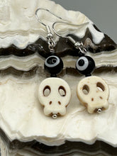 Load image into Gallery viewer, Spooky but festive skull beads with black and white evil eye bead earrings. These stylish skull earrings are perfect for adding a unique flair to any outfit. Whether you're looking for a Dia De Los Muertos accessory or simply looking to draw inspiration, these goth pieces perfectly capture the vampire goth, witchy, dark, Chingona Cabrona, Latina Chicana styles. Measurements: 1” in length