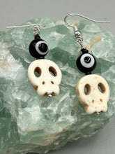 Load image into Gallery viewer, Spooky but festive skull beads with black and white evil eye bead earrings. These stylish skull earrings are perfect for adding a unique flair to any outfit. Whether you're looking for a Dia De Los Muertos accessory or simply looking to draw inspiration, these goth pieces perfectly capture the vampire goth, witchy, dark, Chingona Cabrona, Latina Chicana styles. Measurements: 1” in length