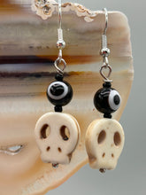 Load image into Gallery viewer, Spooky but festive skull beads with black and white evil eye bead earrings. These stylish skull earrings are perfect for adding a unique flair to any outfit. Whether you're looking for a Dia De Los Muertos accessory or simply looking to draw inspiration, these goth pieces perfectly capture the vampire goth, witchy, dark, Chingona Cabrona, Latina Chicana styles. Measurements: 1” in length