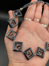 Load image into Gallery viewer, This two-strand necklace, crafted from aqua-blue and silver toned glass beads, is a stunning statement piece. The addition of faceted triangle-shaped glass beads tucked between hematite square beads adds an exquisite and unique flair. The necklace gracefully drapes around the neck, bringing an air of bold and elegant flair to any ensemble it complements. 15” in length, can be extended up to 17"