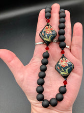 Load image into Gallery viewer, This statement necklace features elegant black matte glass beads with a smooth and velvety finish. Four ornamental ceramic beads with a traditional red, golden, and green pattern create a classic aura and luster-speckled dark red beads bring a striking final touch to the singular look.  This necklace is simple and elegant piece, very versatile look. Perfect cocktail chic attire, fancy wedding necklace, a minimalist look. Necklace: 32” in length Necklace: 32” in length