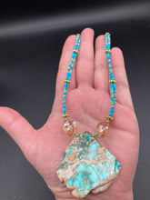Load image into Gallery viewer, This vibrant and striking double strand necklace features a combination of glass beads in blue and green shades of turquoise, gold and champagne. The two delicate strands are accented with a gold-tone flower-shaped bead, a howlite stone chip dyed in turquoise, and shimmery, cross-faceted champagne-colored glass beads to complete the dramatic look. Measurements: Necklace is 17” and can be adjusted up to 19"