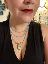Load image into Gallery viewer, This vibrant and enchanting Southwestern Style inspired necklace is comprised of three strands. The first two feature a mix of blue and green turquoise and gold glass beads, while the longest strand features a howlite stone chip dyed turquoise and shimmery cross faceted champaign color glass beads for a dramatic look. Measurements: The Necklace is 16” and can be adjusted up to 18"