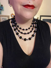 Load image into Gallery viewer, This Bohemian style necklace is composed of three strands of shimmery large black and dark purple glass beads, along with floral metal beads. The elegant drape creates a bold and fierce look that is ideal for a variety of occasions, such as cocktail chic attire and weddings. It is a perfect minimalist accessory.  Measurements:  Necklace is 16” in length - adjustable to 18"
