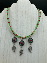 Load image into Gallery viewer, This adjustable necklace features an eye-catching Southwest-inspired design. Multi-hued glass beads, including bright green and vibrant red, are accompanied by dark red and green pendants with silver-plated feather charms. Ideal for chingona guerrera carbonas, la India princesses, warrior cosplay, and native-inspired looks. Measurements: Necklace is 15” adjustable up to 17" in length