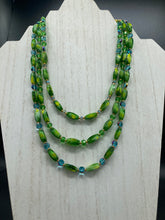 Load image into Gallery viewer, This adjustable glass beaded necklace features a combination of vivid green, blue, and gold hues and a mixture of shapes, creating an eye-catching spectrum of colors and a complex look. The rectangular green glass beads form the predominant part of the three-strand piece, which offers a bold and elegant fashion statement that is ideal for the Spring season. Measurements: Necklace is 17” in length, can be adjusted up to 19" in length