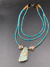 Load image into Gallery viewer, This vibrant and enchanting Southwestern Style inspired necklace is comprised of three strands. The first two feature a mix of blue and green turquoise and gold glass beads, while the longest strand features a howlite stone chip dyed turquoise and shimmery cross faceted champaign color glass beads for a dramatic look. Measurements: The Necklace is 16” and can be adjusted up to 18"