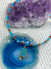 Load image into Gallery viewer, This adjustable choker style necklace features an eye-catching teal wood scarab beetle pendant and glass beaded strands. This dramatic necklace is kept together by double-hole flat matte lava-red beads, providing a collar shape. The necklace artfully wraps around the neck, conveying an elegant and bold style.  Measurements:    Necklace is 14 1/2” in length, can be adjusted up to 16"
