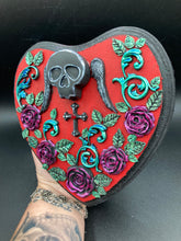 Load image into Gallery viewer, This Memento Mori Wall Art Decor is a one-of-a-kind art piece, skillfully crafted with a black polymer clay skull and wings on a dark red wood frame, decoratively woven with dark red roses and vines. It's perfect for adding an eye-catching touch to any wall and makes a unique, bold gift. Measurements: H 6 3/4" x W 7” x D 1 1/2"