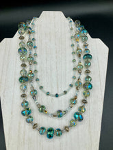Load image into Gallery viewer, This beautiful necklace features shimmery, rich aqua blue and silver tones glass beads. Its three strands consist primarily of faceted rondelle shaped beads, along with a variety of lighter blue and silver beads, resulting in a unique multicolored look. The perfect statement piece, this elegant necklace will drape beautifully across your neck, adding a vibrant hue to any Spring outfit. Measurements: Necklace is 18” in length