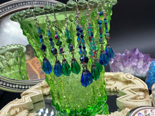 Load image into Gallery viewer, This stunning, one of a kind pair of celestial beaded earrings is a bold addition to any jewelry collection. Crafted with vibrant blue glass beads, the color contains varied shades of blue, purple, and hints of gold to create unique texture. The design is inspired by the awe-inspiring beauty of the majestic galaxy. Measurements: 2” in length