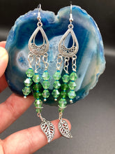 Load image into Gallery viewer, This large set of chandelier earrings features three long strands of shimmering glass beads in various light green and blue hues, accented with an intricate silver-plated leaf charm at the bottom for an added touch of movement. Versatile and perfect for whimsical, hippie-inspired, nature-loving looks. Measurements: 3 3/4” ” in length