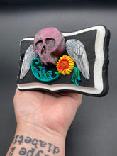 Load image into Gallery viewer, This unique wall art decor, crafted with hand-molded polymere clay and painted on a wooden frame, brings to life a classic Dia De Los Muertos Calavera with its fiery-red skull and bright yellow-orange flower and vine accents. Perfect for accenting your crystal display, witchy altar, or indoor garden.