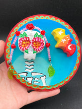 Load image into Gallery viewer, Transform your walls with this handcrafted polymer clay wall art. Showcasing a vibrant Frida Kahlo inspired calavera with hand-beaded floral crown, this Day of the Dead wall decor piece is perfect for adding a traditional Mexican folk art touch to any home.