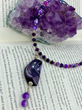 Load image into Gallery viewer, This double-stranded necklace is adorned with a large agate stone displaying a spectrum of purple shades, from light sheer to deep dark tones. The combination of purple agate and multi-colored glass beads makes this pendant a stunning addition to any summer look. Measurements: Necklace is 17” in length