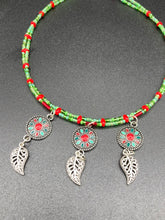 Load image into Gallery viewer, This adjustable necklace features an eye-catching Southwest-inspired design. Multi-hued glass beads, including bright green and vibrant red, are accompanied by dark red and green pendants with silver-plated feather charms. Ideal for chingona guerrera carbonas, la India princesses, warrior cosplay, and native-inspired looks. Measurements: Necklace is 15” adjustable up to 17" in length