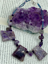Load image into Gallery viewer, This necklace features large trapezoid-shaped Amethyst pendants and small Amethyst nuggets strung together with shimmery multicolored glass beads, creating a unique and eye-catching statement piece. Measurements: Necklace is is 15 1/2” adjustable up to 17"