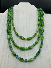 Load image into Gallery viewer, This adjustable glass beaded necklace features a combination of vivid green, blue, and gold hues and a mixture of shapes, creating an eye-catching spectrum of colors and a complex look. The rectangular green glass beads form the predominant part of the three-strand piece, which offers a bold and elegant fashion statement that is ideal for the Spring season. Measurements: Necklace is 17” in length, can be adjusted up to 19" in length