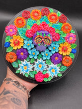 Load image into Gallery viewer, Frida Kahlo inspired calavera with a black wood frame, this Day of the Dead wall decor piece is perfect for adding a traditional Mexican folk art touch to any home. Add a unique touch of style to your home with this intricately detailed, Frida Kahlo-inspired calavera clay wall art. The design features an eye-catching crown of flowers, plus a vibrant bouquet, perfect for any Day of the Dead celebration. Bring a bright and colorful piece of art to your home with this stunning wall hanging.