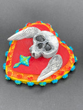 Load image into Gallery viewer, This Memento Mori Wall Art Decor is a unique statement piece to add a pop of color to your walls. Handcrafted with black and white polymer clay, acrylic paint, and a wood frame, the skull artwork is decorated with small turquoise and yellow-orange flowers and a turquoise and gold cross. Perfect for a Day of the Dead altar or a witchy home decor display.