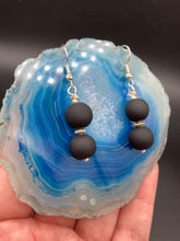Load image into Gallery viewer, These flat matte black glass bead earrings are perfect for creating a cocktail chic ensemble. With a round shape and silver plated floral bead, this timeless piece is ideal for special occasions such as weddings. Its minimalist look exudes effortless elegance. Measurements: 1 1/4” in length