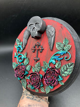 Load image into Gallery viewer, This Memento Mori Wall Art Decor is a one-of-a-kind art piece, skillfully crafted with a black polymer clay skull and wings on a dark red wood frame, decoratively woven with dark red roses and vines. It's perfect for adding an eye-catching touch to any wall and makes a unique, bold gift.  Measurements:  Diameter 6 3/4" x Depth 1 1/2"