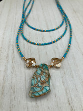 Load image into Gallery viewer, This vibrant and enchanting Southwestern Style inspired necklace is comprised of three strands. The first two feature a mix of blue and green turquoise and gold glass beads, while the longest strand features a howlite stone chip dyed turquoise and shimmery cross faceted champaign color glass beads for a dramatic look. Measurements: The Necklace is 16” and can be adjusted up to 18"