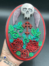 Load image into Gallery viewer, This Memento Mori Wall Art Decor is a one-of-a-kind art piece, skillfully crafted with a black polymer clay skull and wings on a dark red wood frame, decoratively woven with dark red roses and vines. It's perfect for adding an eye-catching touch to any wall and makes a unique, bold gift.  Measurements: H 7" x W 5” x D 1 1/2"