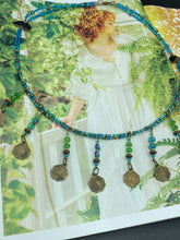 Load image into Gallery viewer, This necklace features vivid green and blue glass beading and a yin yang brass octagon charm. Each side of the charm is distinct, creating a two-in-one look. The look is further enhanced with the addition of rectangular rainbow hematite beads for added visual complexity. Double-hole flat matte gold beads keep the collar shape and add to the necklace's elegant draping when worn.  Measurements:    Necklace is 23” in length