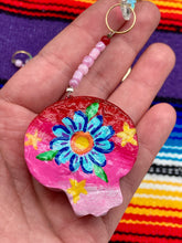 Load image into Gallery viewer, Nature inspired hand crafted polymer clay skull is painted in ombre colors from red, to light pink and decorated with flowers on back and over eyes. Heart rainbow hematite bead on forehead. Light pink glass beaded chain with iridescent crystals. A perfect hanging Day of the Dead art piece to add to your ofrenda, hang next to your display of crystals or witchy altar, add to your skull collection or hang as an art piece on the wall or near a window. Measurements: H 1 1/2” x W 1 1/2” x D 3/4”