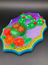 Load image into Gallery viewer, This handcrafted polymer clay wall art features a wood frame painted in a gradient from light to dark purple, creating a stunning sunset look. With a bright green skull cactus plant and bright red blooming flowers, this piece is sure to make a statement. Measurements: H 7" x W 5” x D 1 1/2"