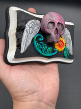 Load image into Gallery viewer, This unique wall art decor, crafted with hand-molded polymere clay and painted on a wooden frame, brings to life a classic Dia De Los Muertos Calavera with its fiery-red skull and bright yellow-orange flower and vine accents. Perfect for accenting your crystal display, witchy altar, or indoor garden.