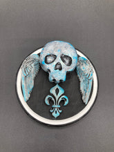 Load image into Gallery viewer, This handcrafted Dia De Los Muertos Calavera wall art decor is a unique way to bring life to your home and celebrates Mexican culture. Made with polymere clay and painted on a wooden frame, the beautiful blue skull is finished with wings and fleur de lis embellishments for a sophisticated look. Perfect for any room! Measurements: D 4"