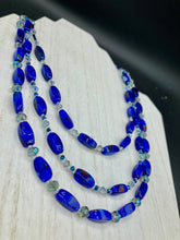 Load image into Gallery viewer, This vibrant royal blue and silver-tone necklace is adjustable and features an eye-catching three-strand design. The rectangular blue glass beads are predominant, complemented by a blend of lighter blue and silver beads for an intriguing multi-hued finish. By mixing shapes and tones, it creates a complex, dimensional look. The draped effect adds a fierce yet elegant pizzazz to any outfit. Perfect for the season of Spring, it will bring a splash of rich color to your wardrobe.