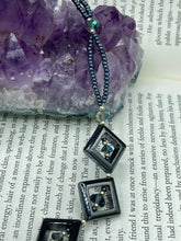Load image into Gallery viewer, This two-strand necklace, crafted from aqua-blue and silver toned glass beads, is a stunning statement piece. The addition of faceted triangle-shaped glass beads tucked between hematite square beads adds an exquisite and unique flair. The necklace gracefully drapes around the neck, bringing an air of bold and elegant flair to any ensemble it complements. 15” in length, can be extended up to 17"