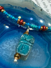 Load image into Gallery viewer, This adjustable choker style necklace features an eye-catching teal wood scarab beetle pendant and glass beaded strands. This dramatic necklace is kept together by double-hole flat matte lava-red beads, providing a collar shape. The necklace artfully wraps around the neck, conveying an elegant and bold style.  Measurements:    Necklace is 14 1/2” in length, can be adjusted up to 16"