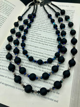 Load image into Gallery viewer, This statement piece features 3 long strands of flat matte black and dark blue glass beads, complemented by a floral metal beaded necklace. It gracefully drapes across the neck for a fierce, yet elegant look, making it perfect for cocktail chic attire, weddings, or minimalist styling.  Measurements:    Necklace is 16” in length - adjustable to 18"