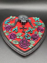 Load image into Gallery viewer, This Memento Mori Wall Art Decor is a one-of-a-kind art piece, skillfully crafted with a black polymer clay skull and wings on a dark red wood frame, decoratively woven with dark red roses and vines. It's perfect for adding an eye-catching touch to any wall and makes a unique, bold gift. Measurements: H 6 3/4" x W 7” x D 1 1/2"
