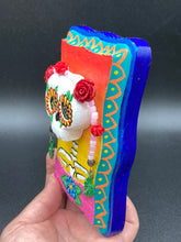Load image into Gallery viewer, Transform your walls with this handcrafted polymer clay wall art. Showcasing a vibrant Frida Kahlo inspired calavera with hand-beaded floral crown, this Day of the Dead wall decor piece is perfect for adding a traditional Mexican folk art touch to any home.