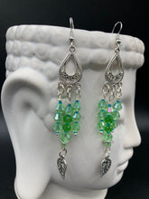 Load image into Gallery viewer, This large set of chandelier earrings features three long strands of shimmering glass beads in various light green and blue hues, accented with an intricate silver-plated leaf charm at the bottom for an added touch of movement. Versatile and perfect for whimsical, hippie-inspired, nature-loving looks. Measurements: 3 3/4” ” in length