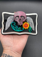 Load image into Gallery viewer, This unique wall art decor, crafted with hand-molded polymere clay and painted on a wooden frame, brings to life a classic Dia De Los Muertos Calavera with its fiery-red skull and bright yellow-orange flower and vine accents. Perfect for accenting your crystal display, witchy altar, or indoor garden.
