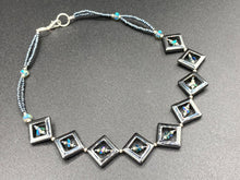 Load image into Gallery viewer, This two-strand necklace, crafted from aqua-blue and silver toned glass beads, is a stunning statement piece. The addition of faceted triangle-shaped glass beads tucked between hematite square beads adds an exquisite and unique flair. The necklace gracefully drapes around the neck, bringing an air of bold and elegant flair to any ensemble it complements. 15” in length, can be extended up to 17"