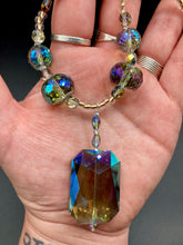 Load image into Gallery viewer, Make a bold statement with this shimmery aqua blue and gold tones glass beaded necklace. The large rectangular faceted shaped pendant creates a vivid contrast to the warm gold tones of the necklace, perfect for adding a rich pop of color to any Spring outfit. The draped design gives this piece an elegant, bohemian look. Measurements: Necklace is 20” in length,