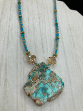 Load image into Gallery viewer, This vibrant and striking double strand necklace features a combination of glass beads in blue and green shades of turquoise, gold and champagne. The two delicate strands are accented with a gold-tone flower-shaped bead, a howlite stone chip dyed in turquoise, and shimmery, cross-faceted champagne-colored glass beads to complete the dramatic look. Measurements: Necklace is 17” and can be adjusted up to 19"