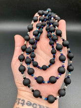 Load image into Gallery viewer, This statement piece features 3 long strands of flat matte black and dark blue glass beads, complemented by a floral metal beaded necklace. It gracefully drapes across the neck for a fierce, yet elegant look, making it perfect for cocktail chic attire, weddings, or minimalist styling.  Measurements:    Necklace is 16” in length - adjustable to 18"