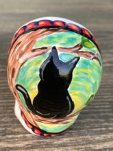 Load image into Gallery viewer, Inspired by nature, ceramic skull is full of vibrant colors and intricate details. The primary color is white with a black cat silhouette and multi-color floral motifs, along with hearts and leaves and lively colorful accents around the entire skull. Mini skull represented the eternal love for a special kitty cat in your life. Black cat silhouette is sitting on a tree branch admiring the starry night sky. Art created for all the cat lovers who adore their sweet kitty. Measurements: H 2 3/4” x W 2” x D 2”