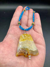 Load image into Gallery viewer, This two-strand necklace features an array of glass beads, including shades of green, blue and turquoise, as well as gold and green. Topped off with a show-stopping yellow agate stone in turquoise, the necklace boasts an eye-catching color combination. Measurements: Necklace is 15 1/2", adjustable up to 17”