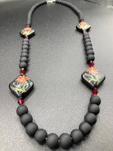 Load image into Gallery viewer, This statement necklace features elegant black matte glass beads with a smooth and velvety finish. Four ornamental ceramic beads with a traditional red, golden, and green pattern create a classic aura and luster-speckled dark red beads bring a striking final touch to the singular look.  This necklace is simple and elegant piece, very versatile look. Perfect cocktail chic attire, fancy wedding necklace, a minimalist look. Necklace: 32” in length Necklace: 32” in length