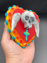 Load image into Gallery viewer, This Memento Mori Wall Art Decor is a unique statement piece to add a pop of color to your walls. Handcrafted with black and white polymer clay, acrylic paint, and a wood frame, the skull artwork is decorated with small turquoise and yellow-orange flowers and a turquoise and gold cross. Perfect for a Day of the Dead altar or a witchy home decor display.